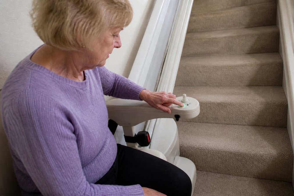 A homeowner checking the battery backup indicator light on a stairlift control panel mounted on the armrest, with clear visibility of the digital display