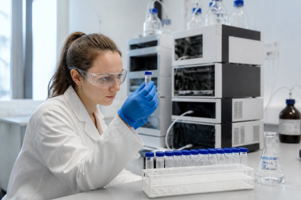 Onderzoeker in laboratoriumjas die standaard peptide-samples in reageerbuisjes onderzoekt, met HPLC-apparatuur en analytische instrumenten op de achtergrond, helder laboratoriumlicht