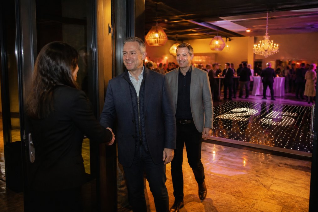 Gasten arriveren bij de ontvangst van een bedrijfsjubileum in een sfeervol verlichte locatie, op de achtergrond is een verlichte dansvloer zichtbaar met het jubileumjaar erin