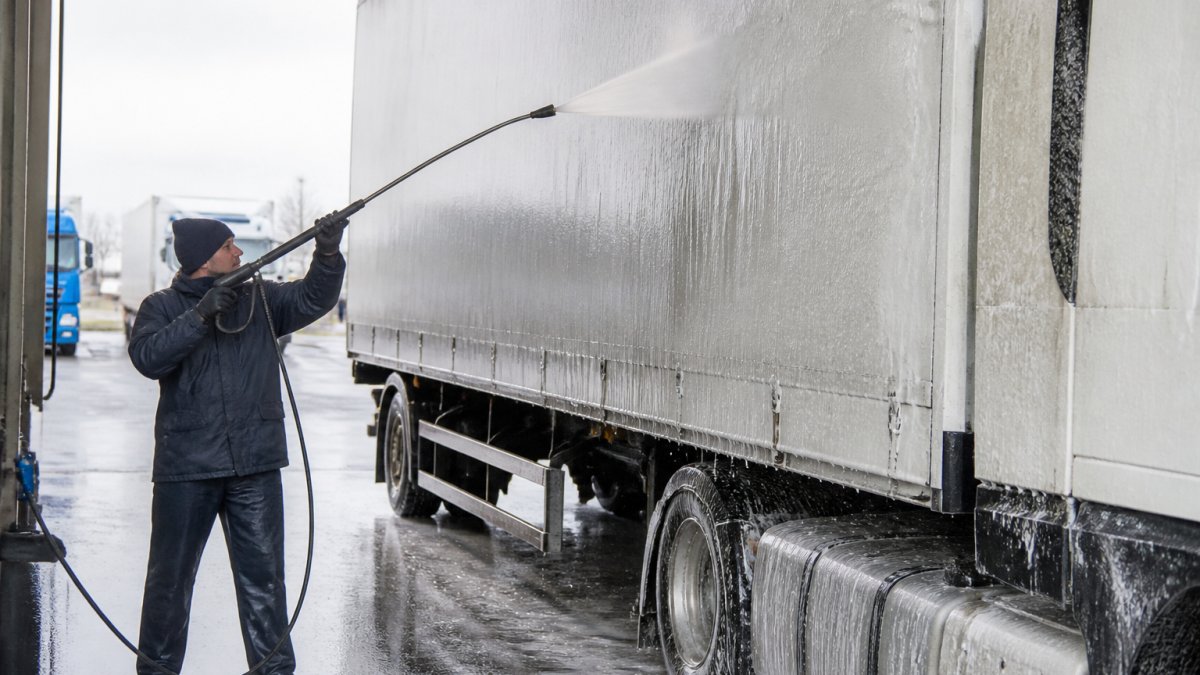 Professionele reiniger brengt schuimende voorwas aan op de zijkant van een vrachtwagen in een wasplaats