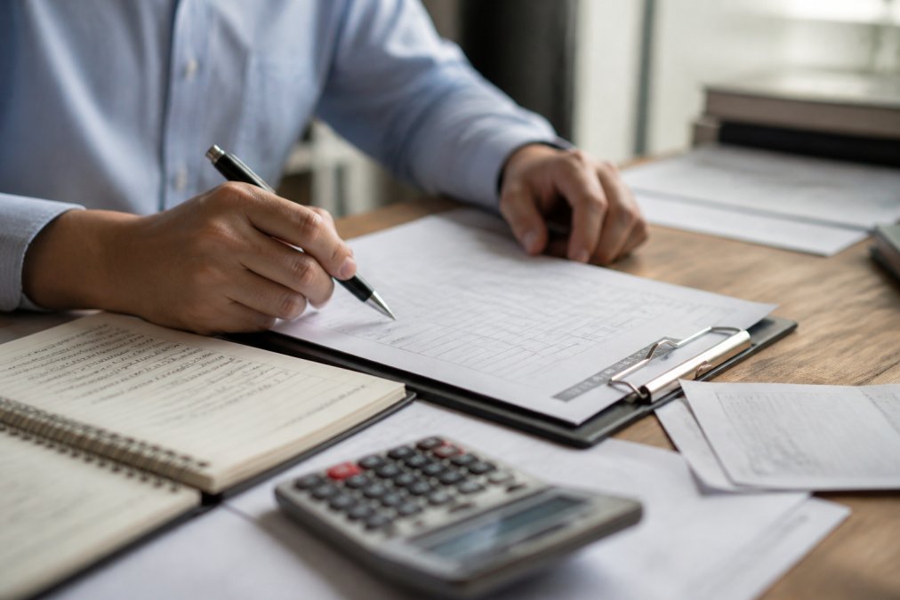 Close-up of a professional's hands reviewing a legal contract at a polished desk, with a pen poised over the document and a notepad with handwritten notes nearby, under warm office lighting