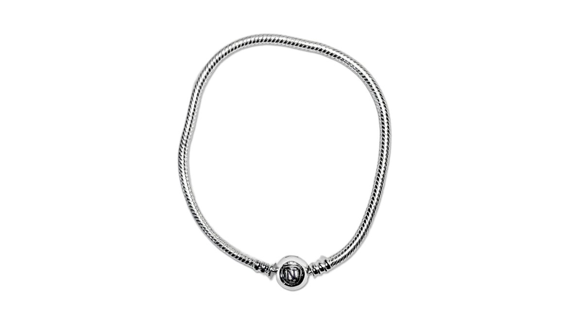 Overhead flat-lay of a sterling silver bangle bracelet surrounded by several small handmade charms, a smart clip, and a lobster clasp on a soft neutral linen background, natural window light