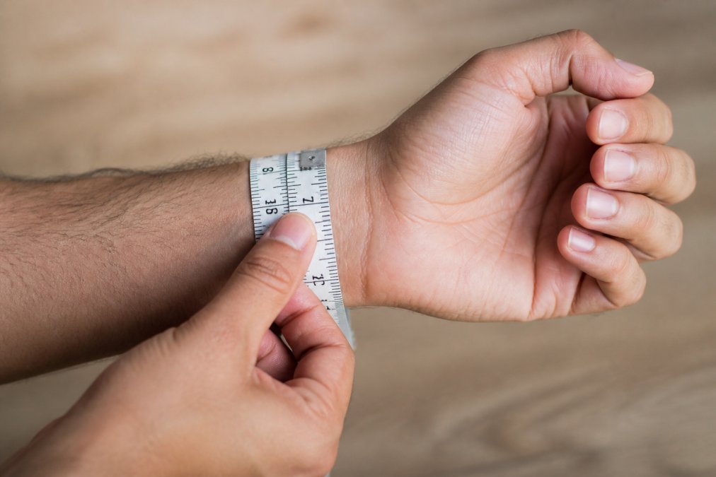 Close-up of a man's wrist with a soft measuring tape wrapped around it at proper position, showing clear measurement markings and relaxed hand position
