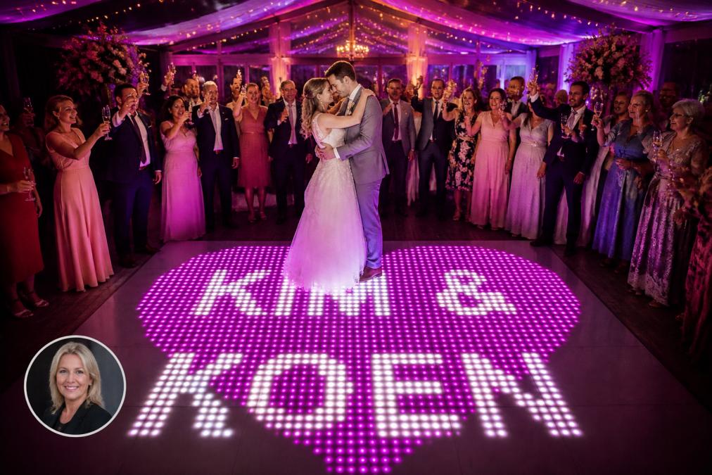 Bruidspaar dansend op een verlichte dansvloer met warm goud en ivoor licht, omringd door feestende gasten met champagneglazen, zachte RGB-verlichting die de bruiloftsdecoratie accentueert
