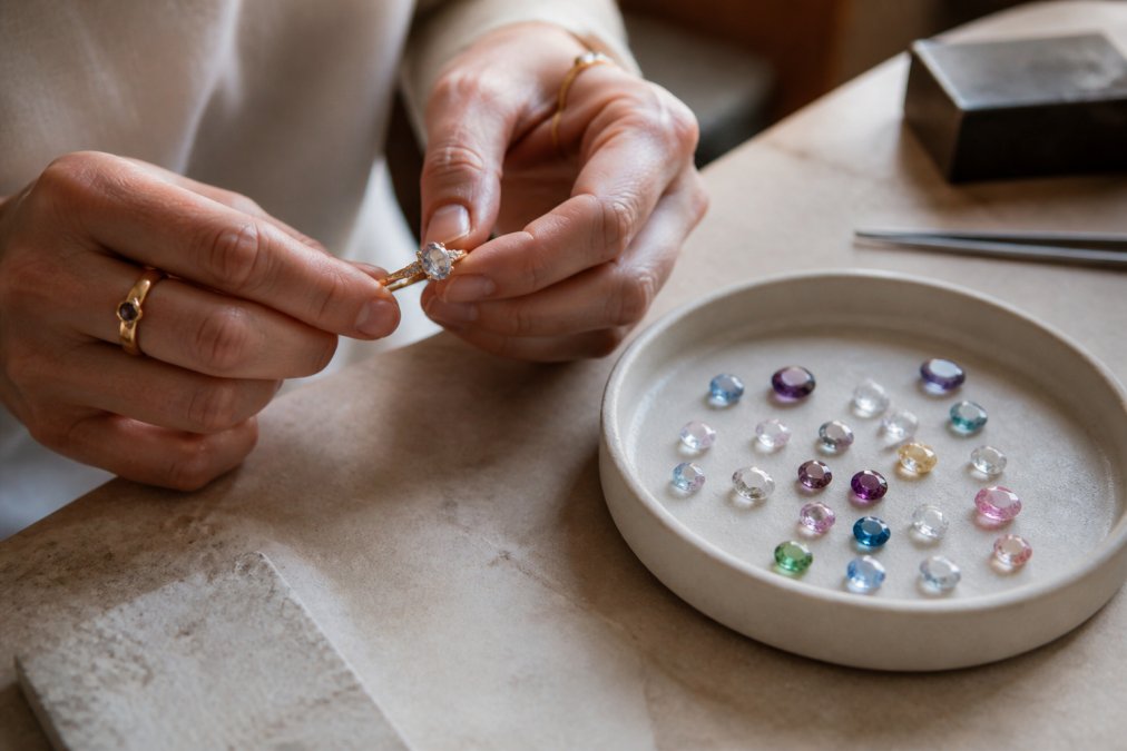 A jeweler holds a delicate ring alongside loose stones, offering a practical alternative to stone river gems.