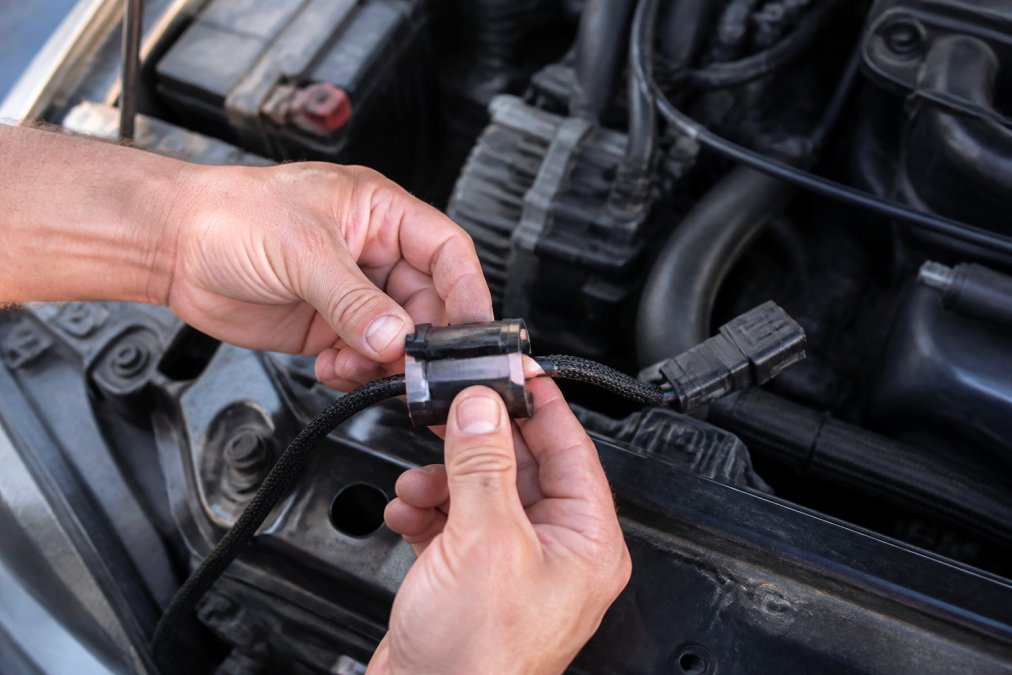 Close-up of a mechanic's hands snapping a ferrite core onto a wire harness near the LED headlight connectors in an open truck engine bay, daylight
