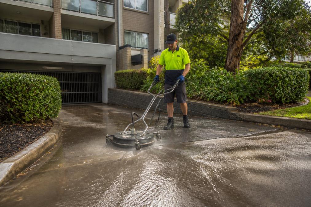 Technician using a surface cleaner for strata driveway cleaning at a residential complex