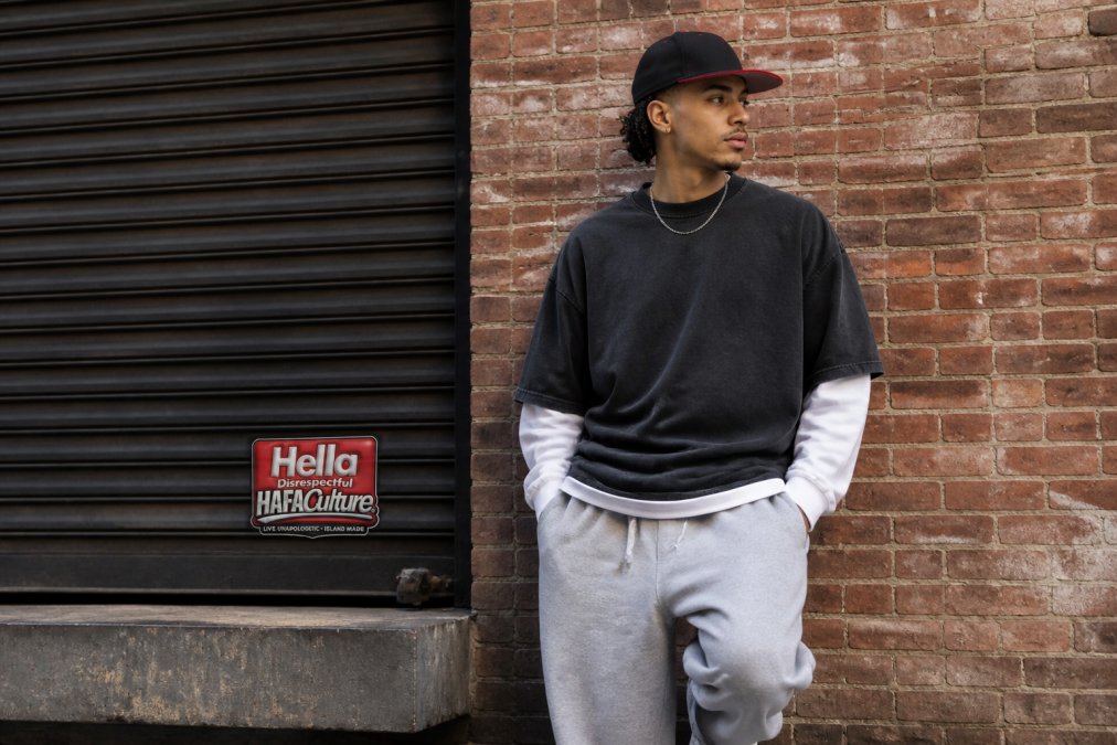 Person in an oversized streetwear brand aesthetic outfit posing confidently against an urban brick wall.