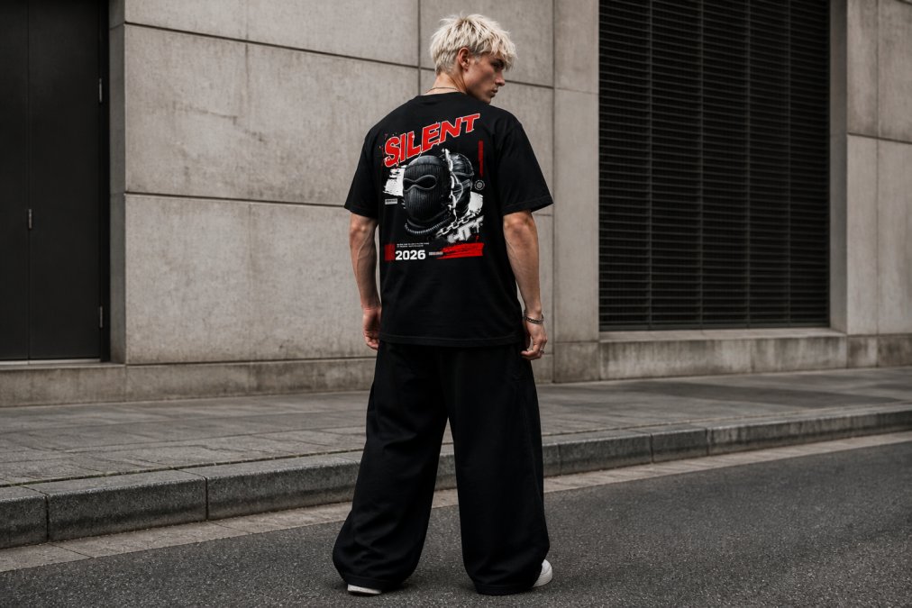 Joven adulto con un conjunto urbano oversize en blanco y negro, pantalones de pierna ancha, camiseta gráfica monocromática y silueta relajada, posando en un entorno urbano con luz natural del día