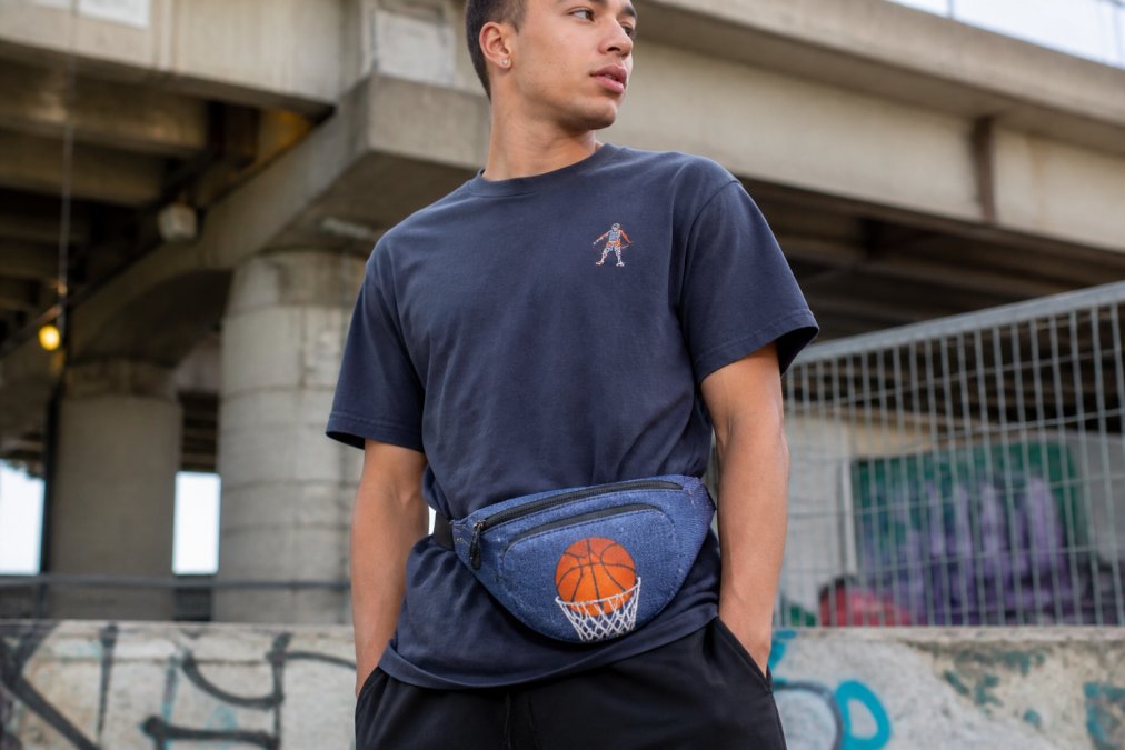 Jongvolwassene draagt een basketbal heuptas in urban streetwear outfit, zichtbaar de details van de tas met geel-wit-zwart design en hoe deze aan de heup zit met casual streetwear look