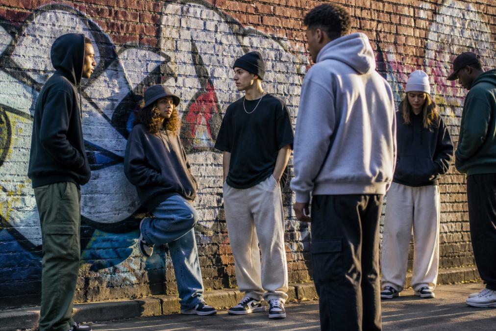 Jongeren in trendy streetwear is fashion outfits met oversized hoodies en sneakers voor een muur met kleurrijke graffiti.