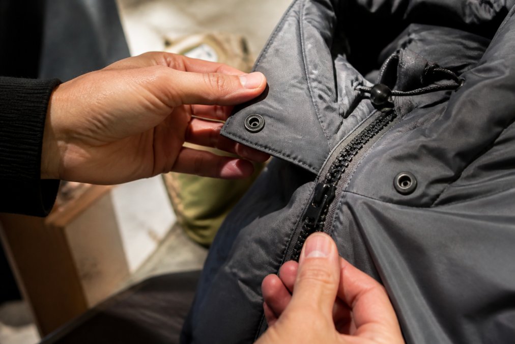 Detail shot van hardware op een streetwear jasje: ritsen, knopen en sluitingen die worden geïnspecteerd op kwaliteit en afwerking tegen helder licht