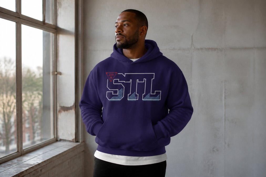 Man in his mid-30s wearing a boxy hoodie and premium tee layered together, standing in natural window light against a neutral backdrop, showing clean silhouettes and visible quality fabric texture