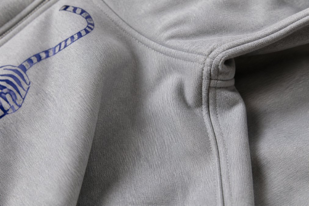 Close-up of premium fabric texture showing tight weave and visible double-stitched seams on a dark cotton hoodie, with detailed view of reinforced shoulder seam and crisp fabric edge under natural lighting