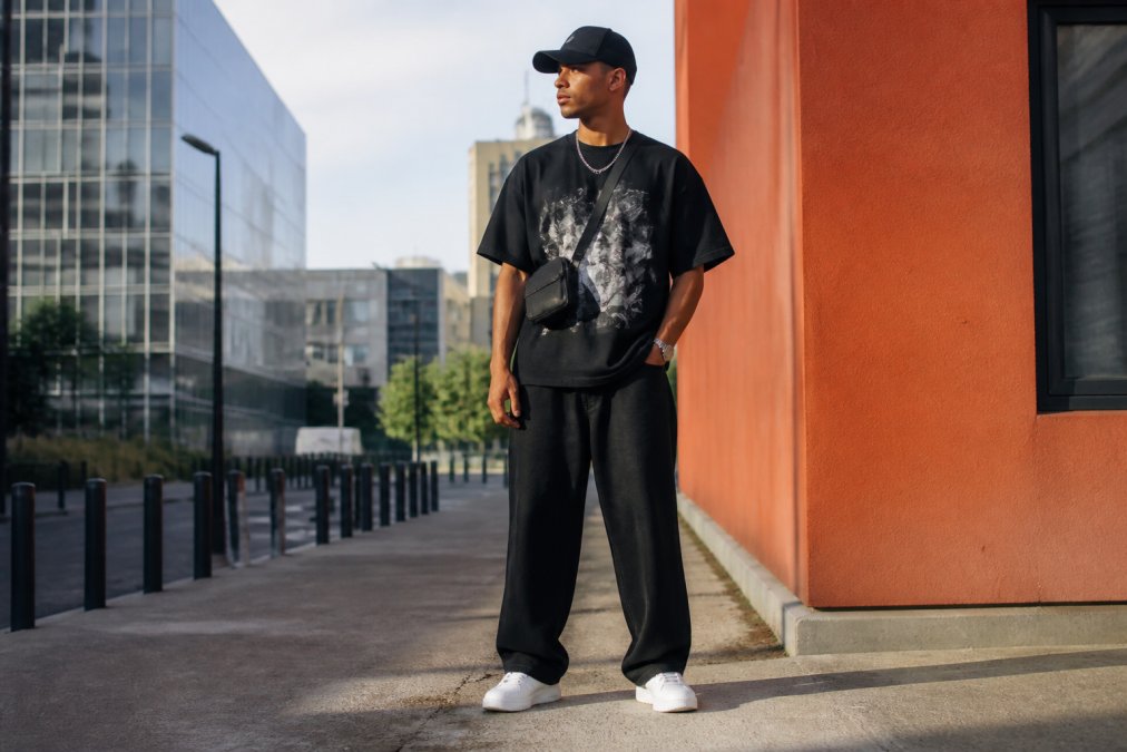 Jongvolwassene in oversized graphic tee en sneakers in een urban setting, geïnspireerd door onze streetwear webshop.