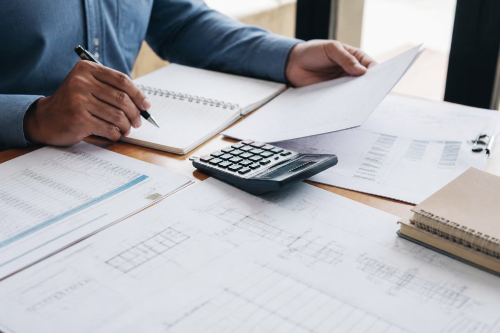 Licensed professional engineer reviewing structural blueprints and stamped drawings at a desk with construction plans spread out, examining calculations and specifications under task lighting