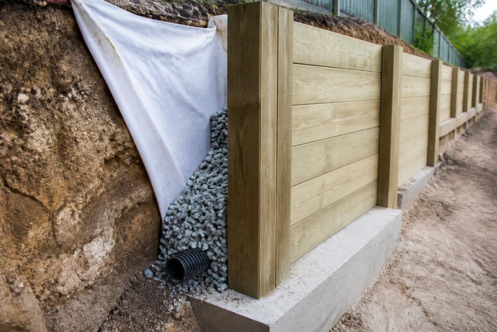 Close-up of a completed retaining wall showing concrete or timber construction with visible footing, backfill and drainage behind the wall on a residential slope