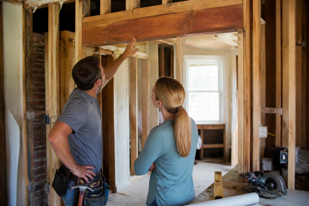 Contractor and homeowner inspecting exposed wall framing and a new header during structural remodeling