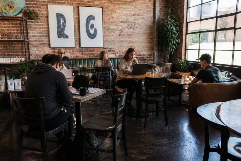 Students studying with laptops and coffee in a bright cafe offering a student discount coffee program.