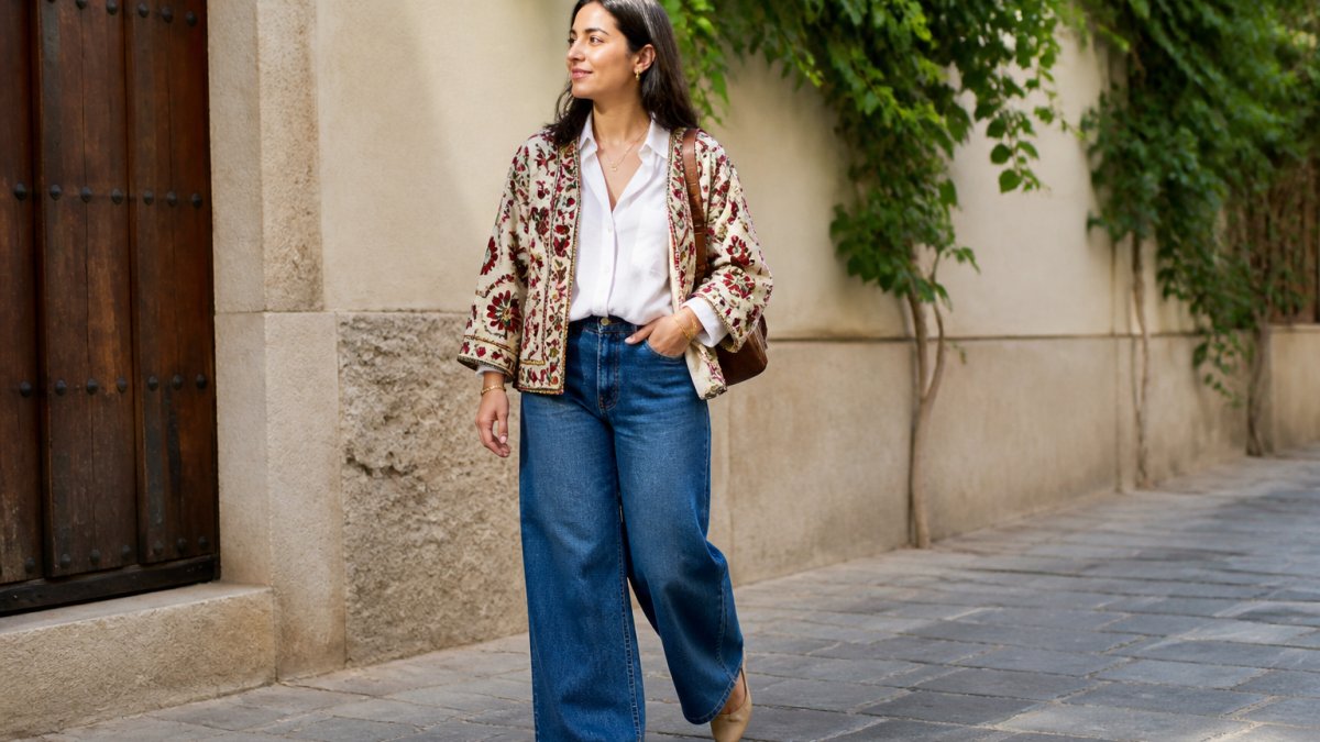 Woman wearing a beaded embellished suzani jacket over a crisp white button-down shirt and wide-leg denim, styled with minimal gold jewelry and neutral leather flats, photographed in natural daylight with soft shadows