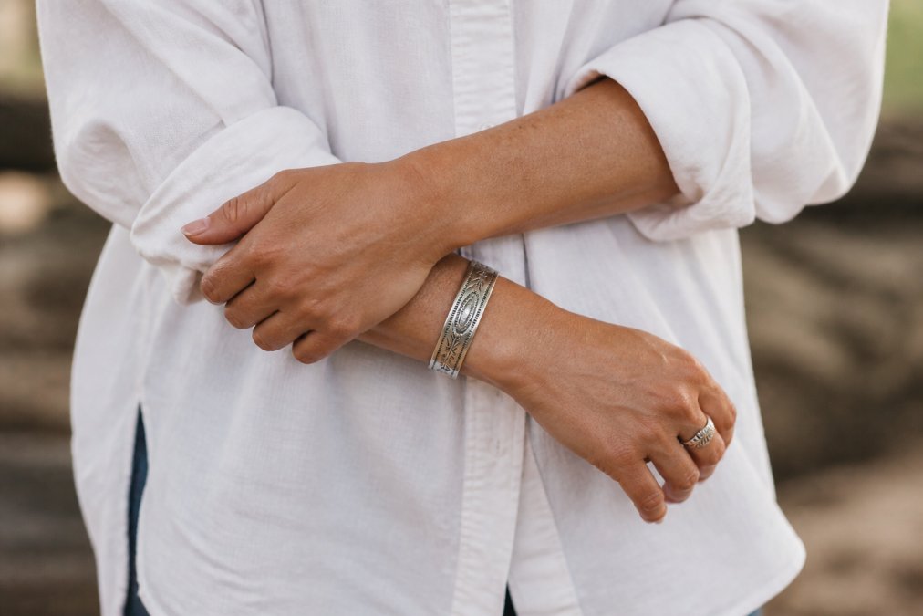 Close-up of wrists wearing a handcrafted sterling silver western cuff paired with a minimalist oversized linen shirt, hands positioned naturally to show how the jewelry sits on the wrist