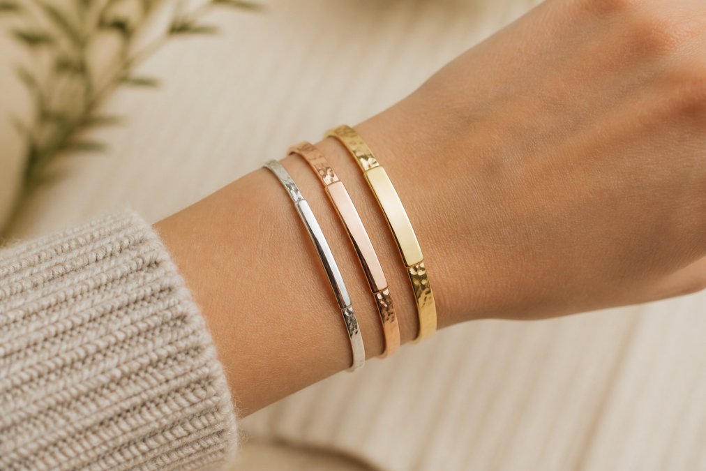 Woman's wrist displaying three stacked engraved bracelets in mixed metals, showing balanced layering with varying widths and finishes against neutral background