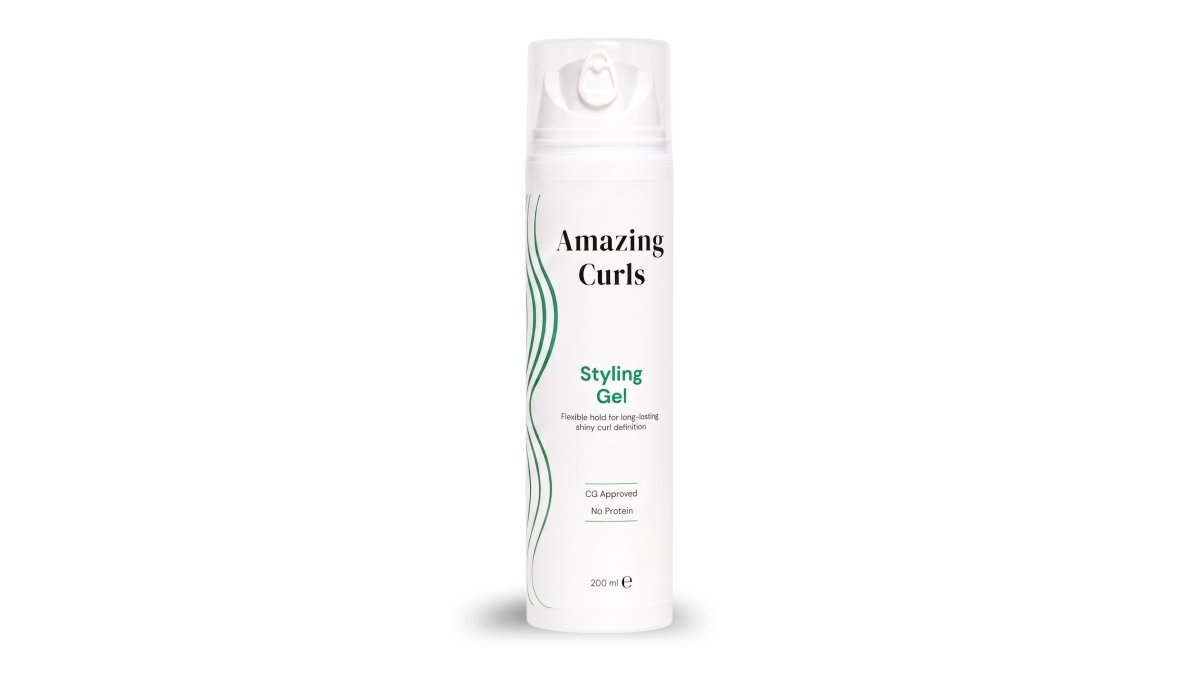 Flat lay van Amazing Curls krullenverzorgingsproducten, waaronder een styling gel, een sealing oil en een gebundelde set, gerangschikt op een wit marmeren oppervlak met een paar losse krullen eromheen, gefotografeerd in helder daglicht
