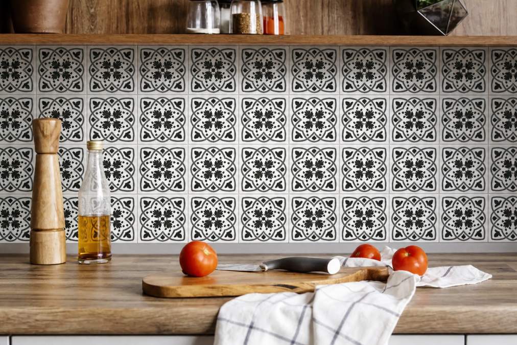 Close-up of a modern kitchen backsplash with charcoal and white scroll peel-and-stick tiles applied in a clean geometric pattern, showing how the tiles transform a plain white wall into a sophisticated focal point with natural morning light