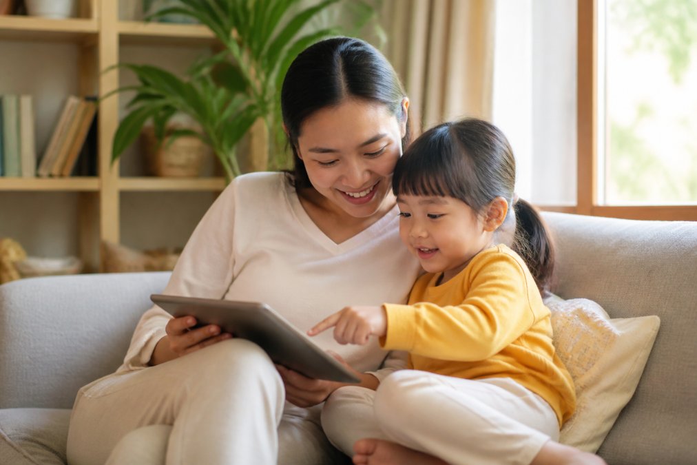 Parent and preschooler sitting on a couch reading colorful educational stories on a tablet together
