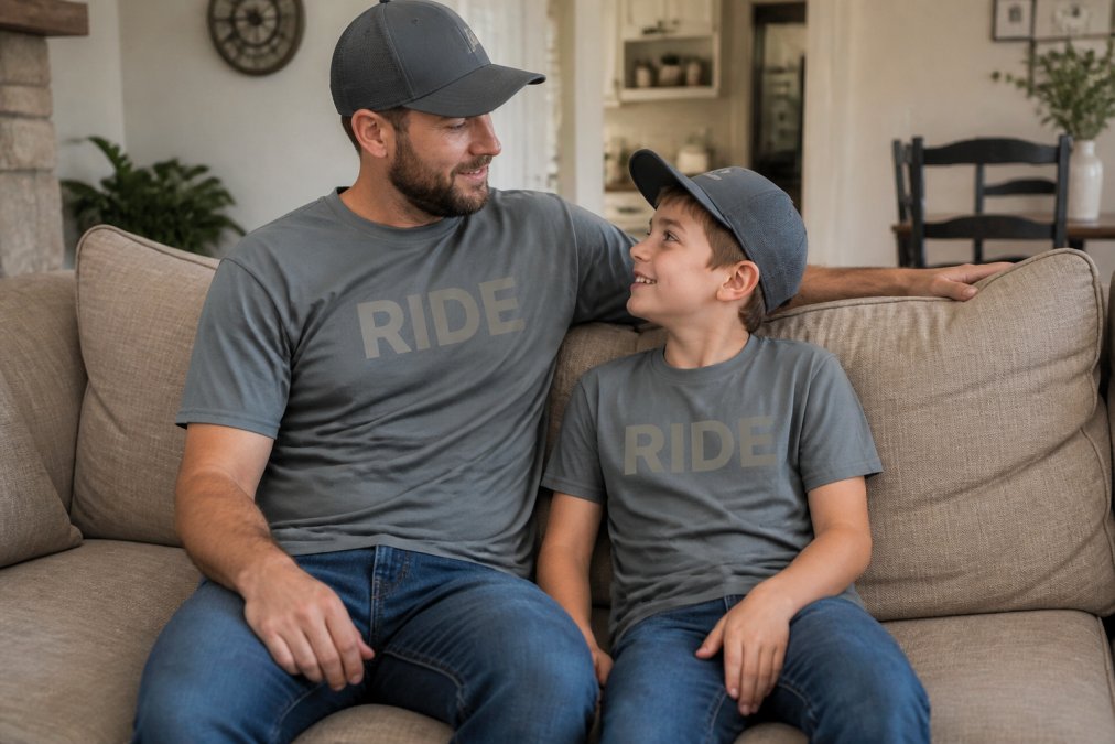 A father and child wearing matching subtle motocross-inspired graphic tees and hoodies in a casual home setting, showing how moto apparel blends family bonding with everyday comfort
