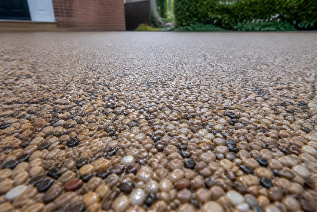 Close-up of a newly installed resin bound driveway with water droplets on the surface, showing the permeable texture and finish with natural light highlighting the aggregate stones