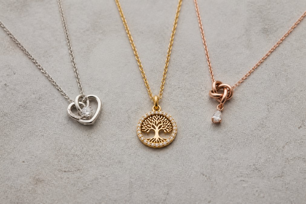 Flat lay of three different personalized necklaces on a neutral background, each with distinct metal finishes and pendant styles, showing variety in design approaches