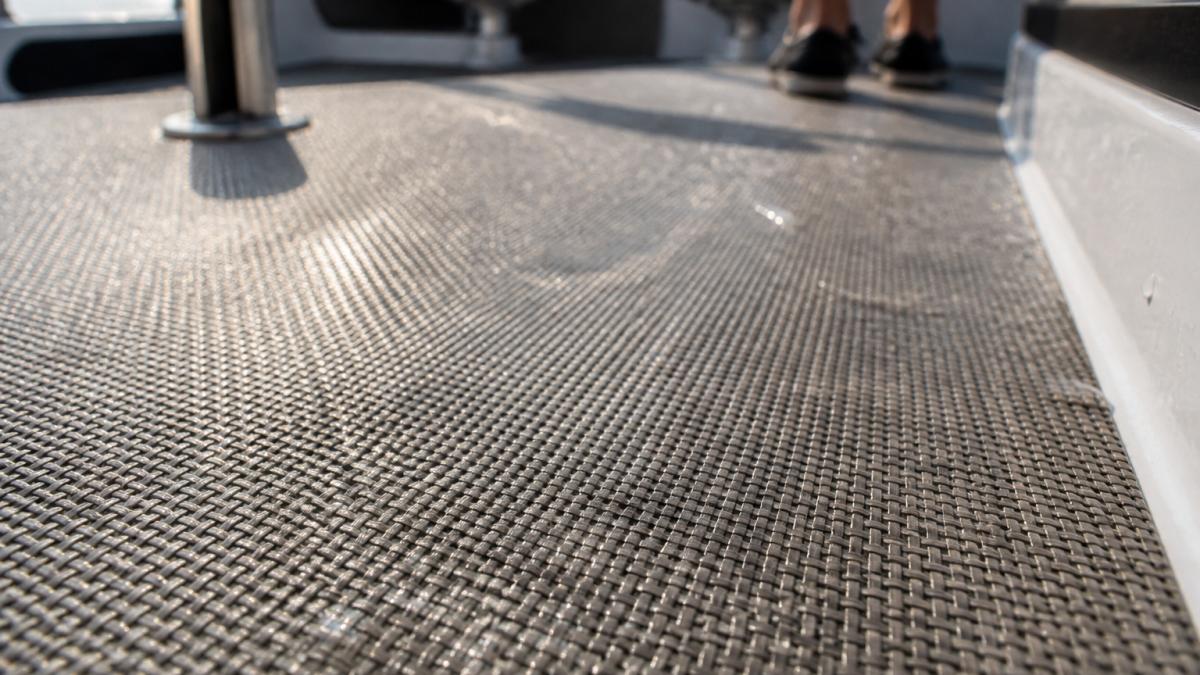 Close-up of woven vinyl flooring on boat deck showing texture detail, light foot traffic wear patterns, and water droplets on the surface in natural sunlight