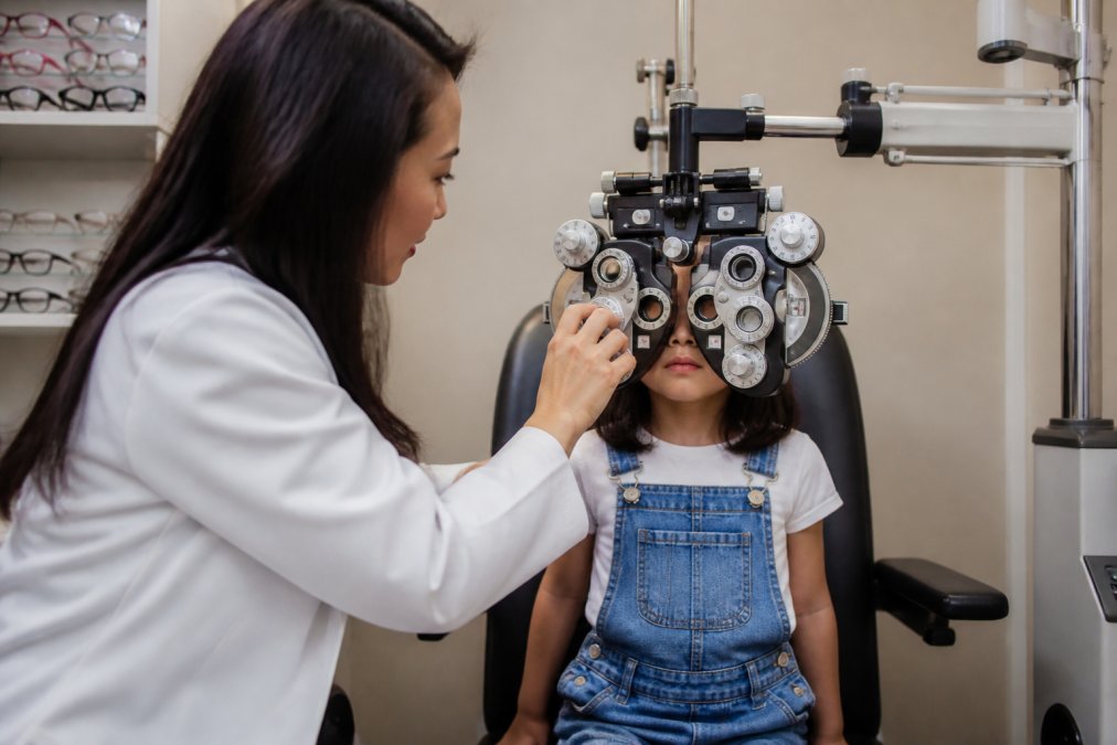 Optometrist performing comprehensive eye examination on a young child using advanced phoropter equipment in a bright clinical setting
