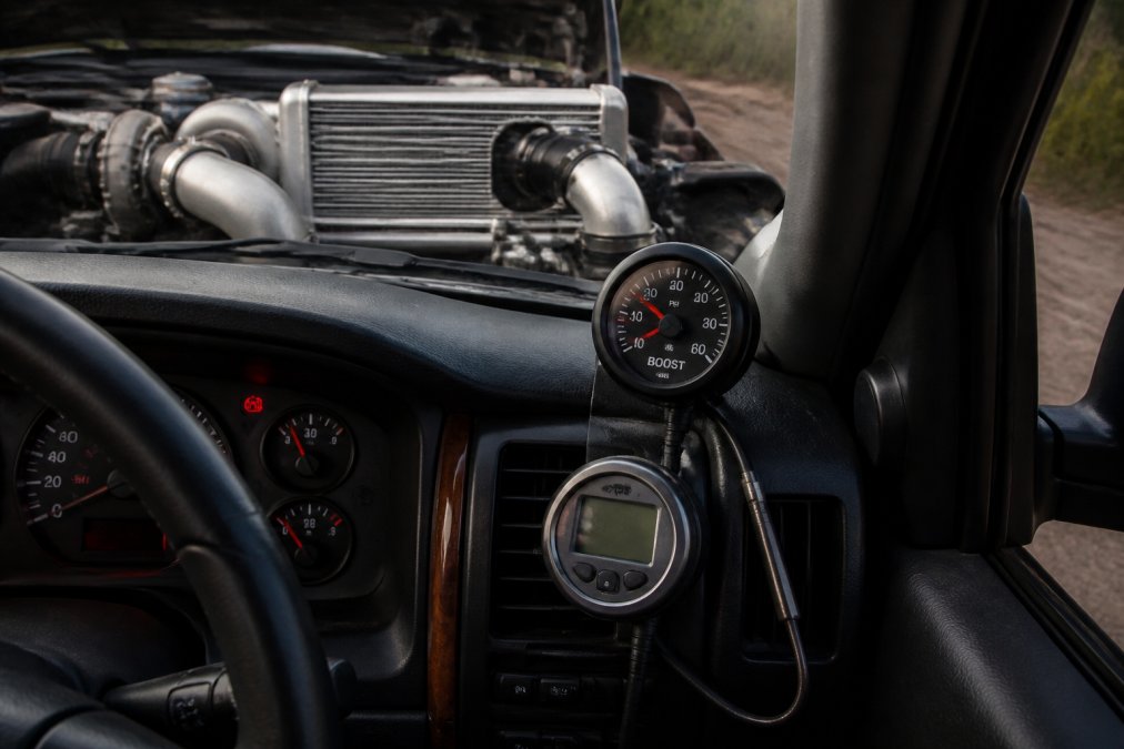 Close-up of diesel engine bay with visible intercooler, boost pressure gauge, and EGT pyrometer installed on dashboard, showing thermal management components in a well-organized truck cab