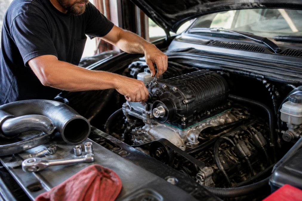Mechanic installing a bolt-on supercharger kit on a pickup truck engine bay to explain supercharger vs turbocharger