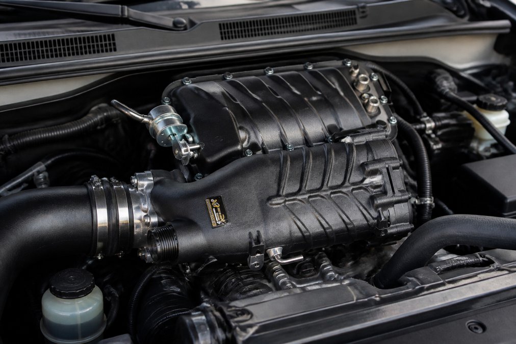 Close-up of a 4Runner engine bay with a twin-screw supercharger mounted on the intake manifold, showing the polished aluminum housing and connected air intake components in professional shop lighting