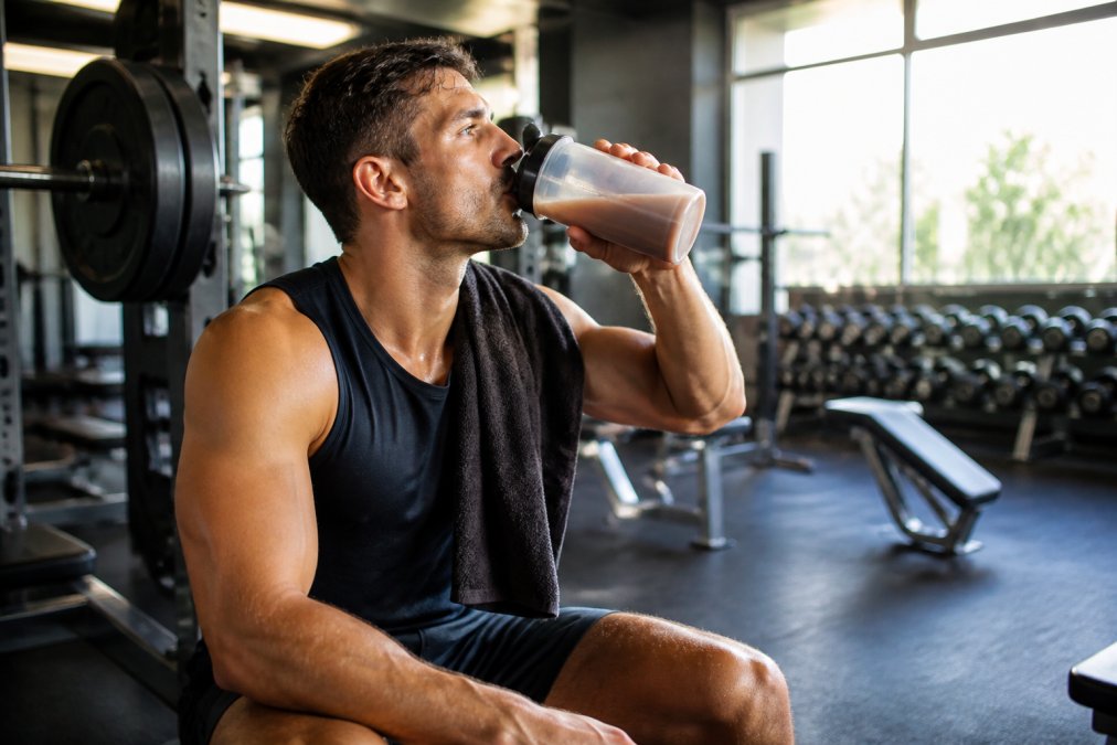 Athlete drinking a post-workout shake to aid supplements to help with muscle recovery in a sunlit gym.