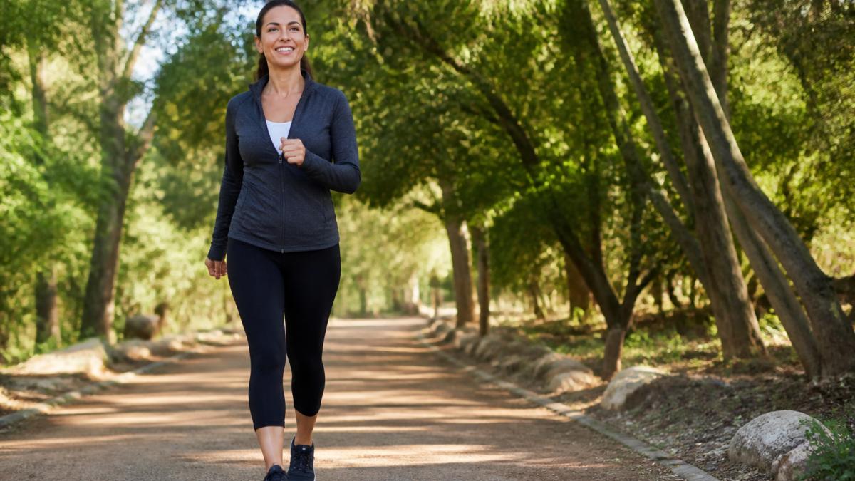 Active adult performing brisk walking outdoors on a tree-lined path in natural daylight, showing steady movement and engaged posture