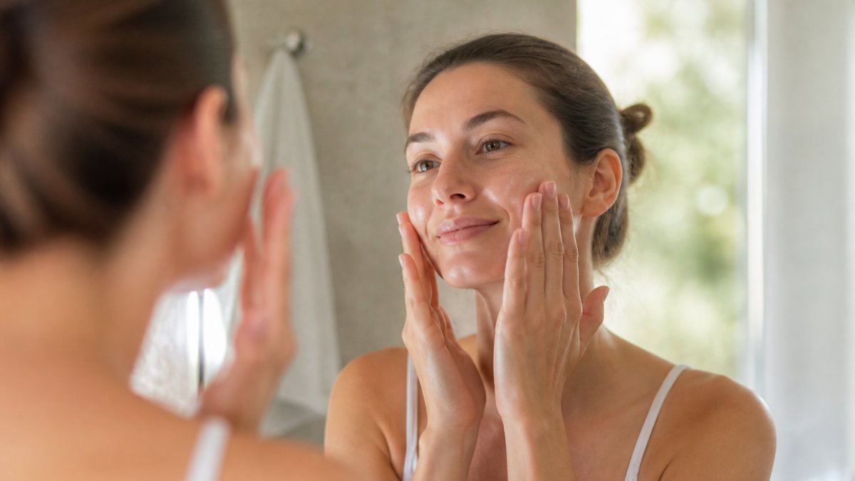 Woman applying hydrating serum to her face with fingertips, showing gentle upward motions on clean, bare skin with soft natural lighting
