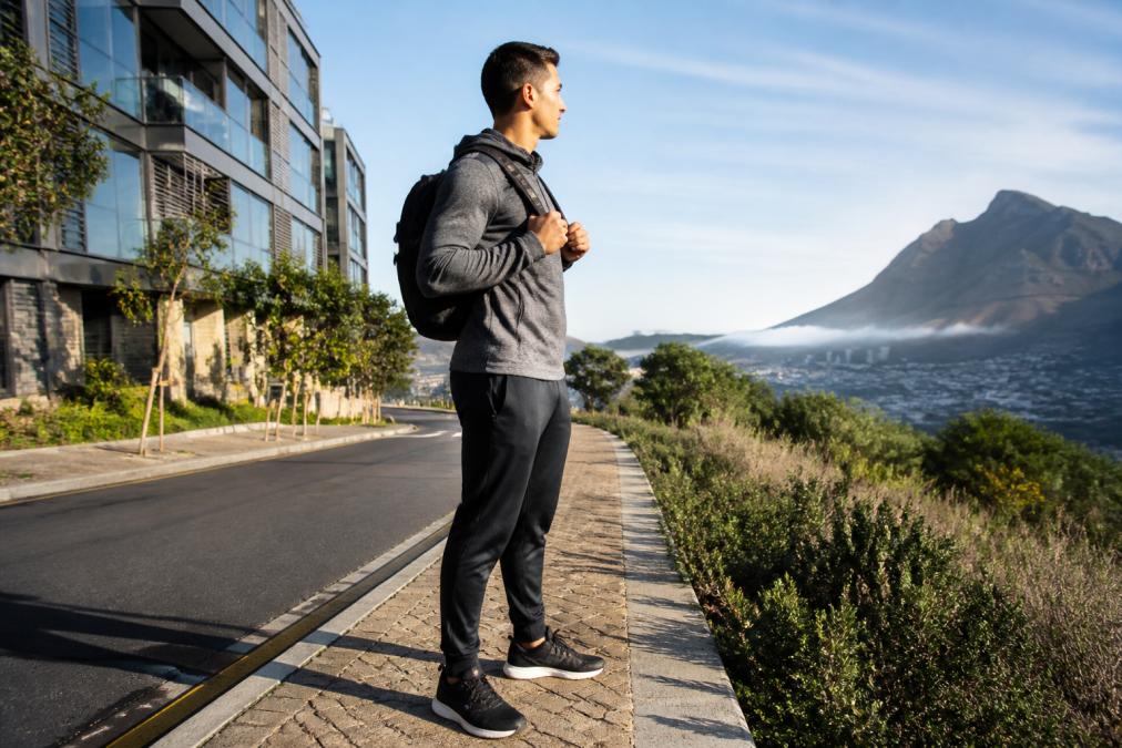 Man wearing sustainable athletic clothing standing on a city sidewalk with mountain trails in the distance.