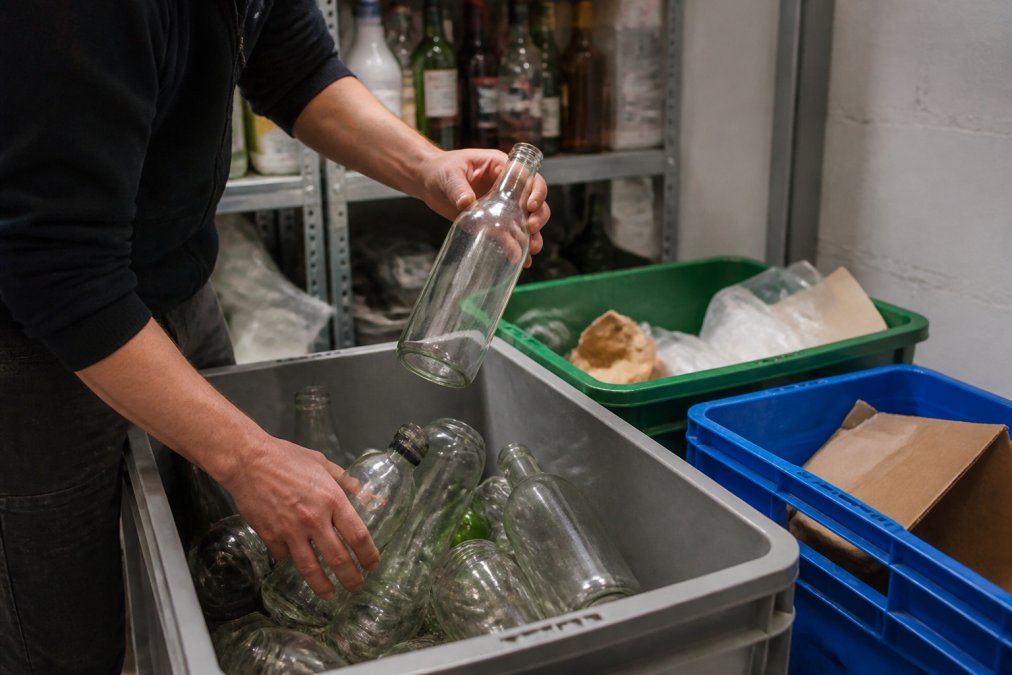 Close-up of hands sorting recyclable glass bottles and packaging materials into separate containers in a hotel bar stockroom