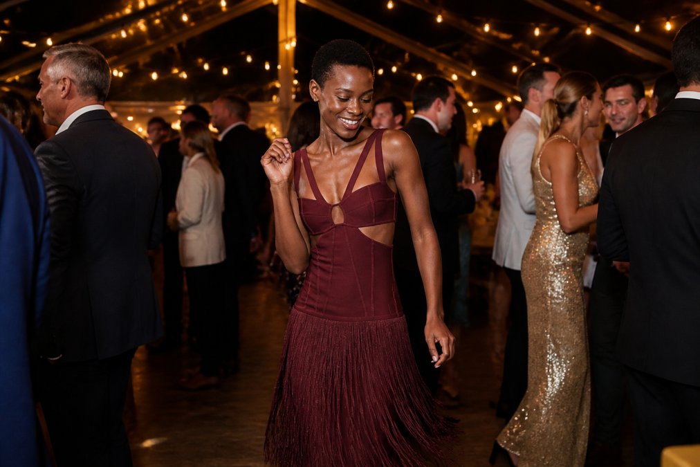 Woman in an elegant sustainable formal dress at a wedding reception, standing confidently while dancing, with soft evening light catching the fabric's texture and detail