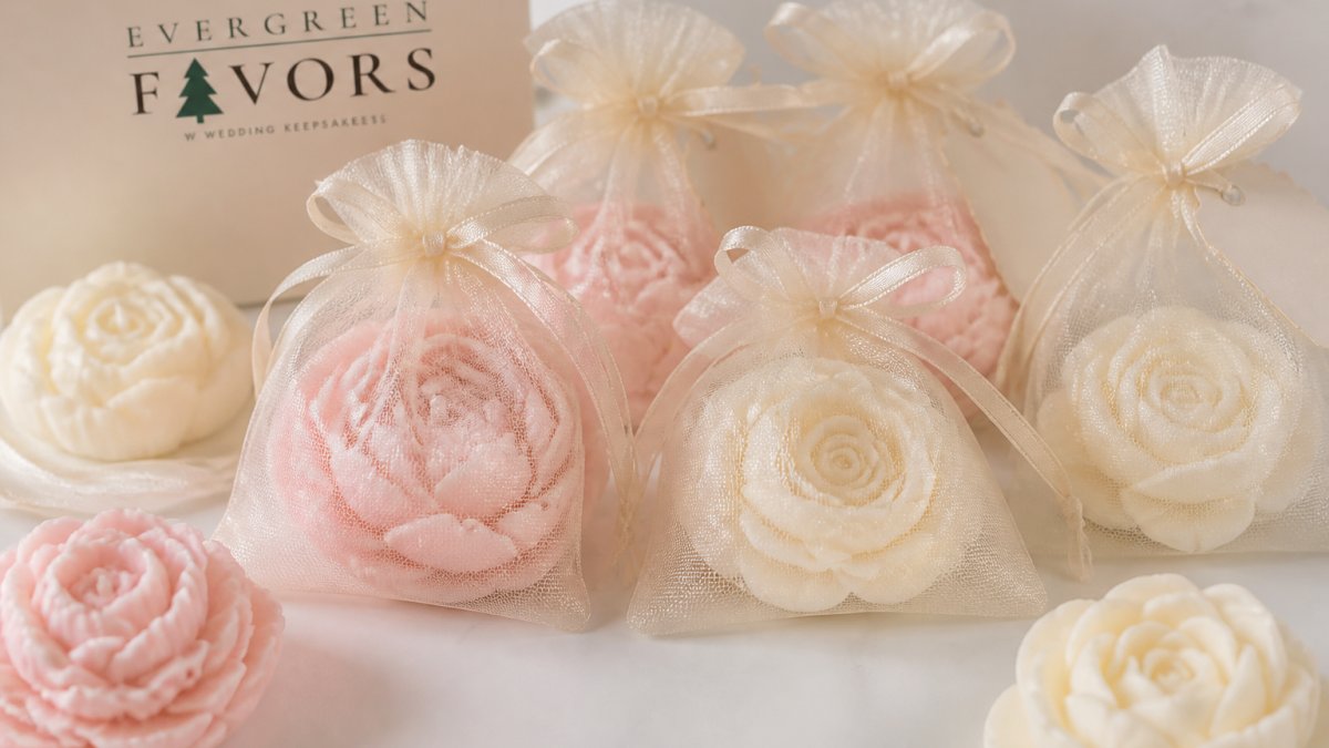 Close-up of elegantly wrapped peony and rose soy wax candles in soft pastel colors, arranged on a white table with delicate organza bags and personalized favor tags
