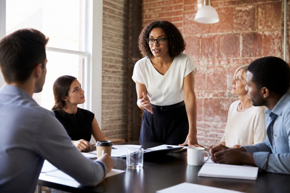 Professional demonstrating tailored behavioral training for teams technique in modern office setting with diverse professionals engaged in collaborative discussion around a table