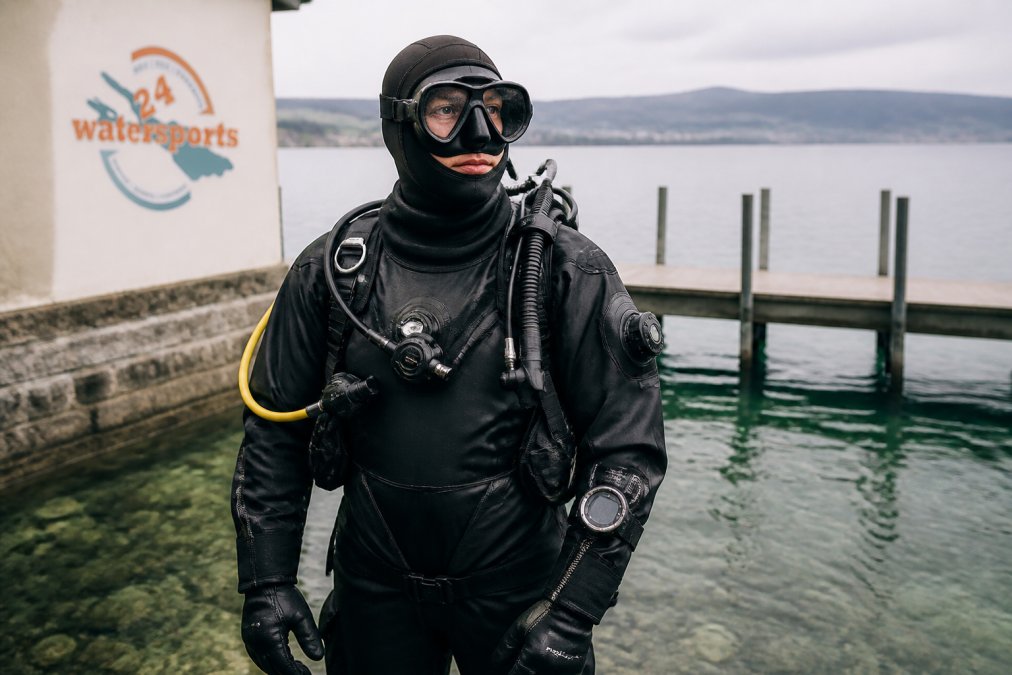 Ein Taucher in vollständiger Ausrüstung mit Trockentauchanzug, Atemregler und Tauchcomputer, bereit für einen Tauchgang im klaren Wasser