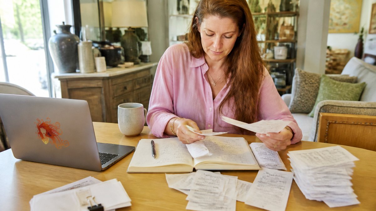 Person organizing receipts, invoices, and digital transaction records on a desk with laptop and notebook showing household item sales documentation