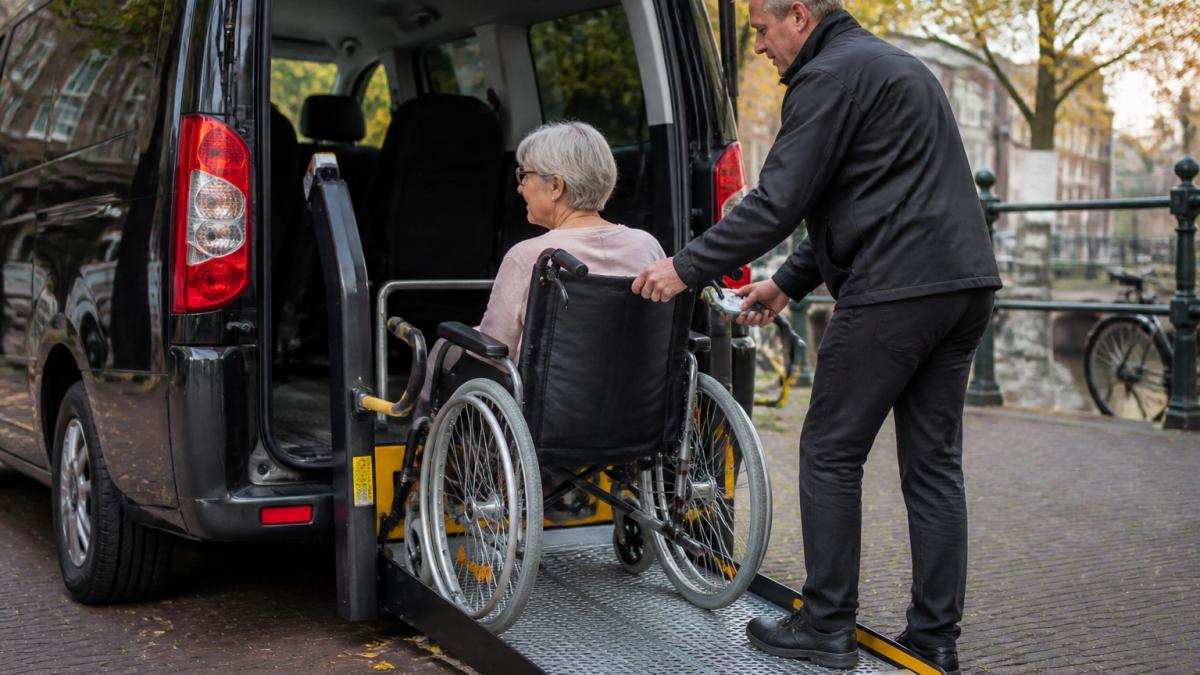 Ervaren chauffeur helpt rolstoelgebruiker veilig in een aangepaste rolstoeltaxi met zichtbare rolstoellift en bevestigingssysteem, natuurlijke daglicht
