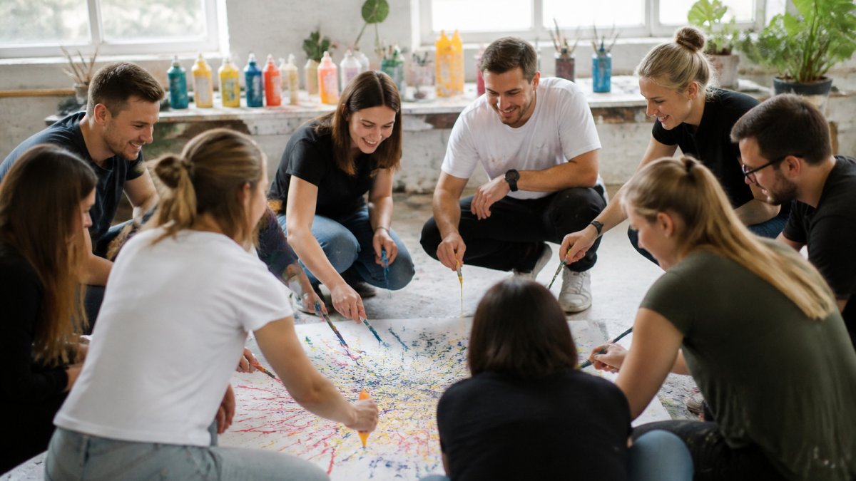 Ein kleines Team von etwa 8-10 Personen sitzt in einem Kreis in einer hellen, modernen Umgebung und führt gemeinsam eine interaktive Übung durch, alle konzentriert und lächelnd