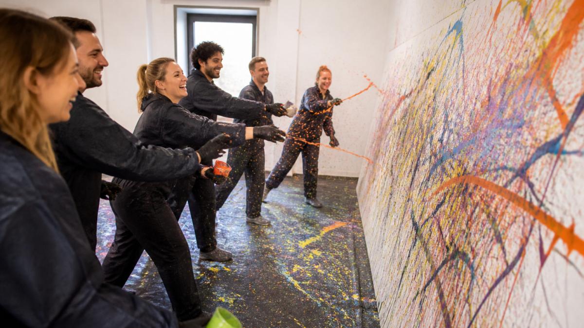 Lachendes Team beim kreativen Mal-Workshop für Teambuilding Wien indoor in einem hellen, farbigen Atelier.